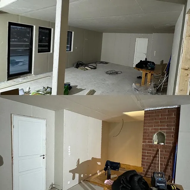 Et uferdig rom med lyse vegger, to store vinduer, en hvit dør, og byggematerialer liggende på gulvet.