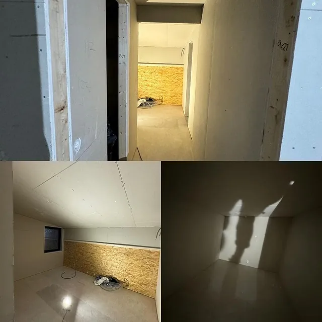 En smal gang med lysmalte vegger, som fører til et rom med panel av kryssfiner på den bakre veggen.