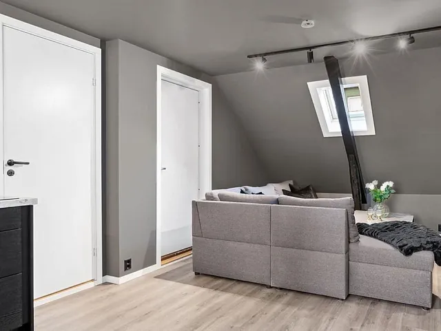 Lyst oppholdsrom med gråe vegger og skråtak. En grå sofa står i bakgrunnen.